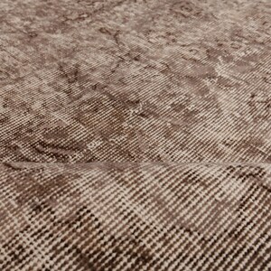May include: Close-up of a vintage-style rug with a distressed pattern. The rug features a blend of brown and beige tones, with a textured surface and subtle variations in color. The design has a classic, aged appearance.