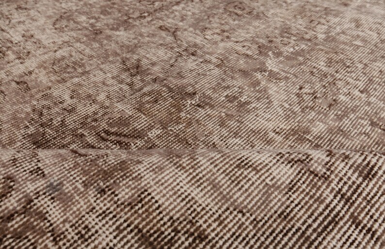 May include: Close-up of a vintage-style rug with a distressed pattern. The rug features a blend of brown and beige tones, with a textured surface and subtle variations in color. The design has a classic, aged appearance.