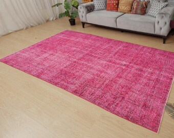 May include: A large, rectangular rug in a vibrant fuchsia colour. The rug has a distressed, vintage appearance with variations in the colour, creating a textured effect. The rug is placed on a light-coloured wooden floor.