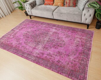 May include: A rectangular area rug featuring a vibrant magenta and deep purple colour palette with a distressed, faded floral medallion pattern. The rug has a dark border with intricate detailing and a low-pile texture covering the floor surface.