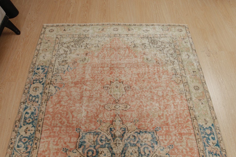 Puede incluir: Una alfombra vintage con un fondo melocot&oacute;n descolorido y un patr&oacute;n floral azul y beige. La alfombra tiene un aspecto desgastado y descolorido y un borde con flecos.