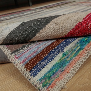 Może przedstawiać: Kolorowy, ręcznie tkany dywan w pasy w odcieniach czerwieni, błękitu, zieleni, brązu i bieli. Dywan jest złożony na pół, odsłaniając skomplikowane detale tkactwa.