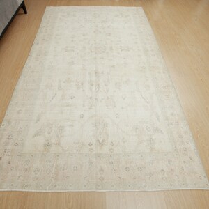 以下が含まれることがあります： くすんだ花柄の入った、クリーム色のヴィンテージラグ。ラグは使い込まれたような風合いがあり、柔らかな天然繊維でできています。