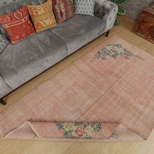 May include: A light pink vintage rug with a floral design. The rug is rolled up and has a light brown background.