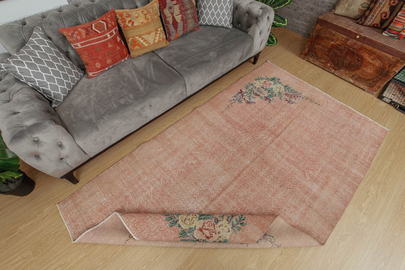 May include: A light pink vintage rug with a floral design. The rug is rolled up and has a light brown background.