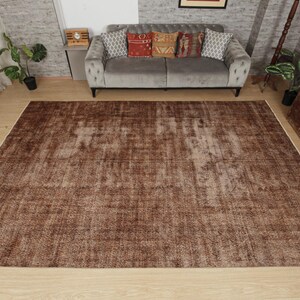 May include: A large rectangular area rug featuring a distressed, weathered texture in various shades of brown. The rug has a low-pile surface with a faded, mottled appearance, showcasing a uniform color palette across its entire flat surface.