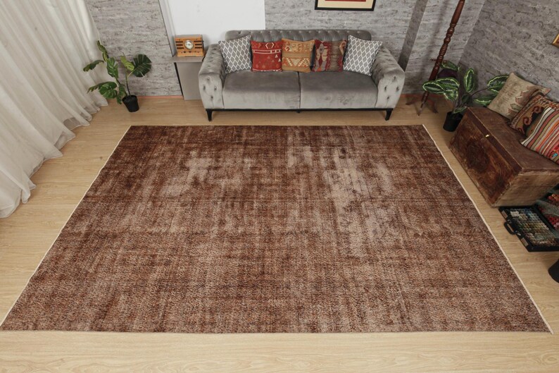 May include: A large rectangular area rug featuring a distressed, weathered texture in various shades of brown. The rug has a low-pile surface with a faded, mottled appearance, showcasing a uniform color palette across its entire flat surface.