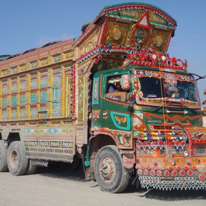 May include: A brightly decorated green HINO truck with intricate painted designs and colorful embellishments. The truck has a large cargo bed with multiple compartments and is adorned with numerous lights and ornaments.