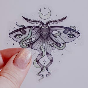 Könnte beinhalten: Aufkleber mit einer detaillierten Illustration einer Motte mit schlangenartigen Anhängseln und Augen auf ihren Flügeln. Das Design beinhaltet einen Halbmond und Sterne, mit einer Farbpalette aus Grau, Lila und Grün.