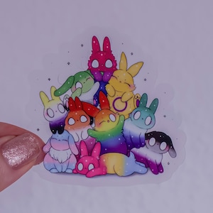 Könnte beinhalten: Ein gestanzter Aufkleber mit einer Gruppe von zehn Cartoon-Hasen in verschiedenen Farben und Mustern, darunter Regenbogen-, Rosa-, Gelb-, Grün- und Blauverläufe, alle verziert mit kleinen weißen Sternakzenten auf transparentem Grund.