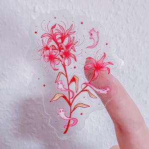 May include: A clear sticker featuring a cluster of vibrant red spider lily flowers with long, delicate stamens. Intertwined among the stems and petals are several small, pale pink, ghost-like creatures with simple facial features and long, flowing tails.