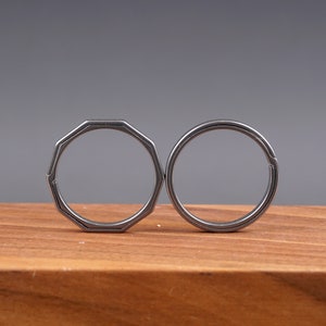 Puede incluir: Dos llaveros plateados, uno con forma redonda y el otro con forma octogonal, se muestran sobre una superficie de madera.