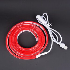 May include: A coiled red LED strip light with a white interior and a white USB cable. The light has a white switch and a USB connector. The light is on a black background.