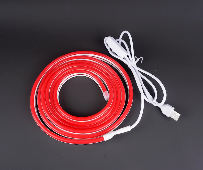 May include: A coiled red LED strip light with a white interior and a white USB cable. The light has a white switch and a USB connector. The light is on a black background.