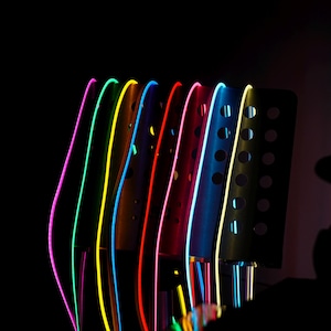 May include: A row of colorful, curved metal objects with neon lights. The lights are in shades of pink, green, yellow, blue, and red. The metal objects have a dark, matte finish and a series of circular cutouts.