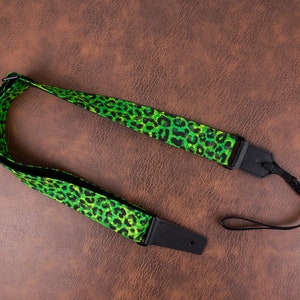 Puede incluir: Una correa de cámara verde y negra con un diseño de estampado de leopardo. La correa tiene longitud ajustable y una correa de muñeca desmontable.