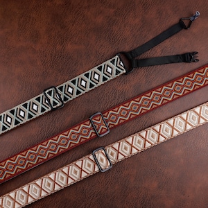 May include: Three patterned straps with black hardware. The top strap is black and gray with diamond shapes. The middle strap is red with a geometric pattern. The bottom strap is tan with diamond shapes. The straps are on a brown leather-like surface.