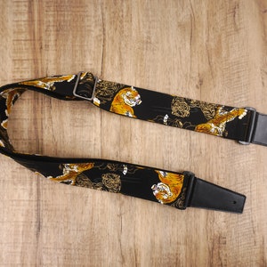 May include: Black guitar strap with a tiger print design. The strap has black leather ends with adjustable buckles.
