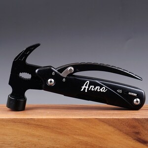 Op de afbeelding: Zwarte multitool met een hamerkop, tang en een mes. De tool is gegraveerd met de naam "Anna".
