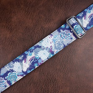 May include: A fabric strap featuring a repeating pattern of white and light blue koi fish interspersed with blue, white, and purple floral motifs. The strap includes a rectangular silver-toned metal slider for length adjustment and stitching.