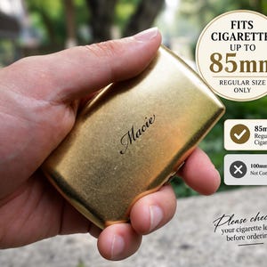Puede incluir: Una pitillera de metal dorado con acabado cepillado y el nombre Macie grabado en letra cursiva. La pitillera está etiquetada para cigarrillos de hasta 85 mm de longitud, con indicadores claros de compatibilidad solo para tamaño estándar.