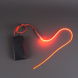 May include: A black battery pack with red and black wires connected to a glowing orange neon light. The neon light is in a curved shape. The background is a solid grey colour.