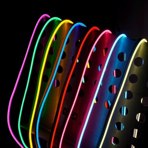 May include: A close-up of a modern, abstract design featuring curved metal elements with vibrant neon lights. The lights are arranged in a rainbow of colors, including pink, green, yellow, orange, red, blue, and white, against a black background.