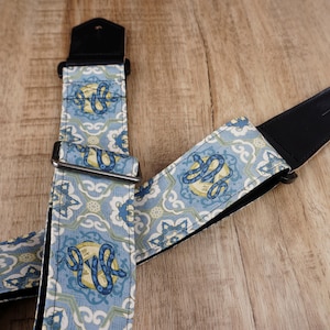Könnte beinhalten: Ein Gitarrengurt mit einem blauen und weißen Muster, das ein Schlangenmotiv zeigt. Der Gurt hat schwarze Lederenden und silberne Metallbeschläge.