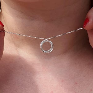 May include: A silver necklace with a delicate chain and a double circle pendant. The pendant is made of two intertwined circles, each with a small, sparkly detail.