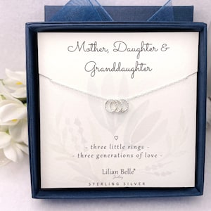 May include: A sterling silver necklace with three interlocking rings, presented in a navy blue gift box with a matching ribbon. The card inside reads "Mother, Daughter & Granddaughter" and "three generations of love."