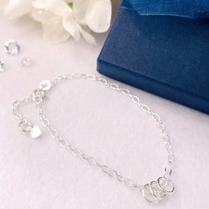 May include: A silver chain bracelet with a heart charm and three interlocking rings.