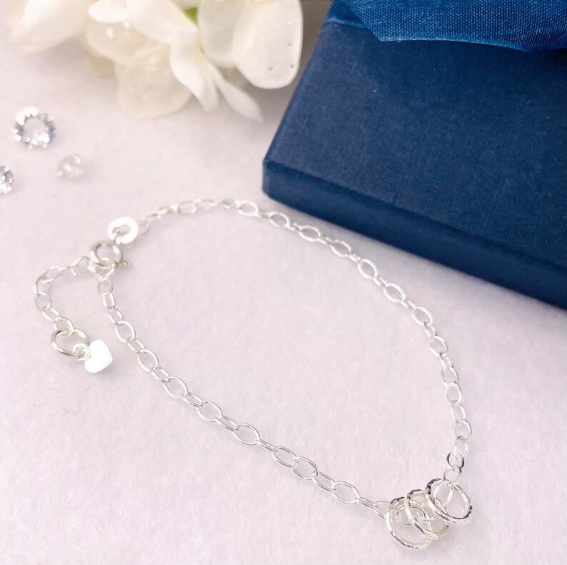 May include: A silver chain bracelet with a heart charm and three interlocking rings.
