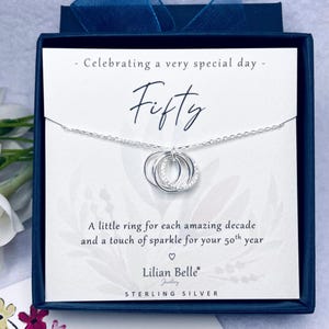May include: Sterling silver necklace with three interlocking rings, one encrusted with small crystals, presented in a navy blue gift box. The card reads "Celebrating a very special day - Fifty".