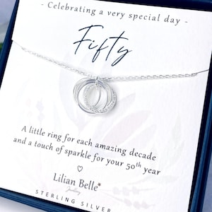 May include: A sterling silver necklace with three interlocking rings, one encrusted with small clear stones, hangs on a card that reads "Fifty." The card also says "Celebrating a very special day" and "Lilian Belle Jewellery."