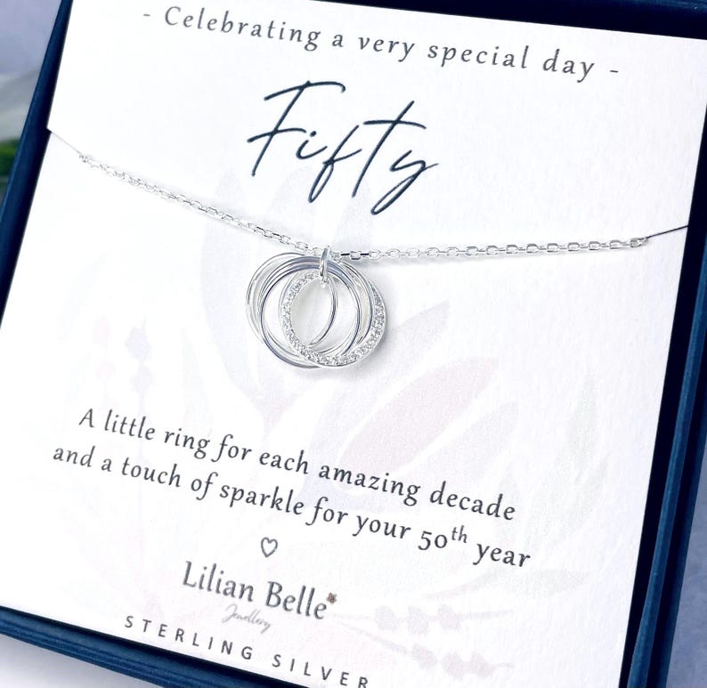 May include: A sterling silver necklace with three interlocking rings, one encrusted with small clear stones, hangs on a card that reads "Fifty." The card also says "Celebrating a very special day" and "Lilian Belle Jewellery."