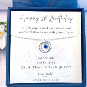 May include: A silver necklace with a blue sapphire birthstone and two rings, presented in a blue box with a card that reads "Happy 21st Birthday. A little ring to mark each decade and your birthstone to celebrate your 21st year. - SAPPHIRE - symbolising CALM, PEACE & TRANQUILITY. Lilian Belle Jewellery STERLING SILVER."