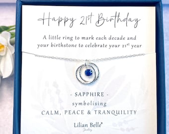 May include: A silver necklace with a blue sapphire birthstone and two rings, presented in a blue box with a card that reads "Happy 21st Birthday. A little ring to mark each decade and your birthstone to celebrate your 21st year. - SAPPHIRE - symbolising CALM, PEACE & TRANQUILITY. Lilian Belle Jewellery STERLING SILVER."