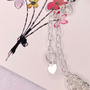 May include: Silver charm bracelet with a heart charm and multiple circular charms. The bracelet has a lobster clasp closure.