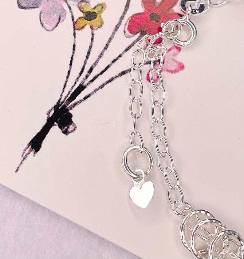 May include: Silver charm bracelet with a heart charm and multiple circular charms. The bracelet has a lobster clasp closure.