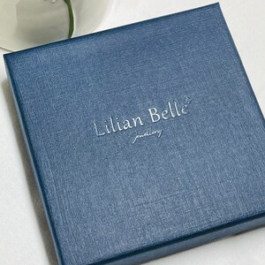 May include: A navy blue jewelry box with the text "Lillian Belle Jewelry" embossed in silver lettering.