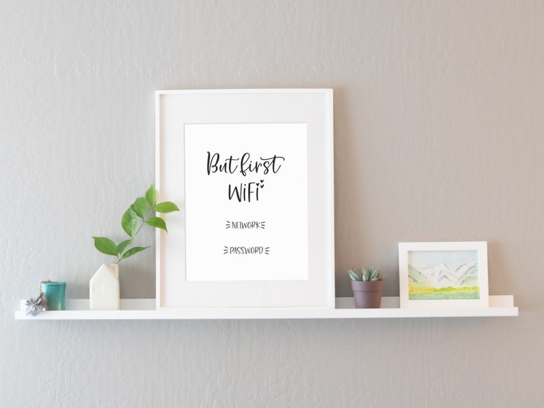 May include: White framed print with the text "But first WiFi" and blank lines for network and password. The print is on a white shelf with a small potted plant and a teal candle.