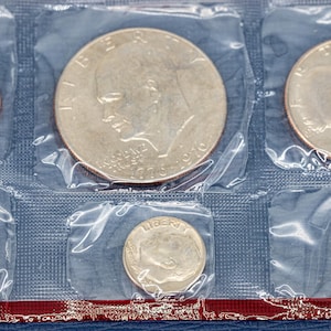 May include: A collection of U.S. coins, including a half dollar, quarter, dime, nickel, and penny, sealed in clear plastic. The coins are arranged in a grid pattern. The set is presented against a blue background.