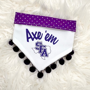 May include: White dog bandana with a purple polka dot trim and black pom-poms. The bandana features the text "Axe 'em" in purple script, along with the SFA logo.