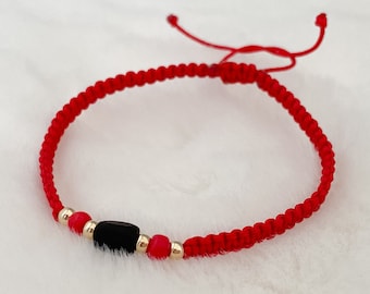 Puede incluir: Pulsera de cuerda roja con una cuenta negra y cuentas doradas.