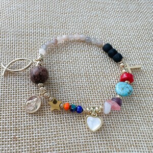 May include: A gold bracelet with a variety of charms, including a fish, a star, a heart, a cross, and several colorful beads. The bracelet is made of gold metal and has a delicate chain.
