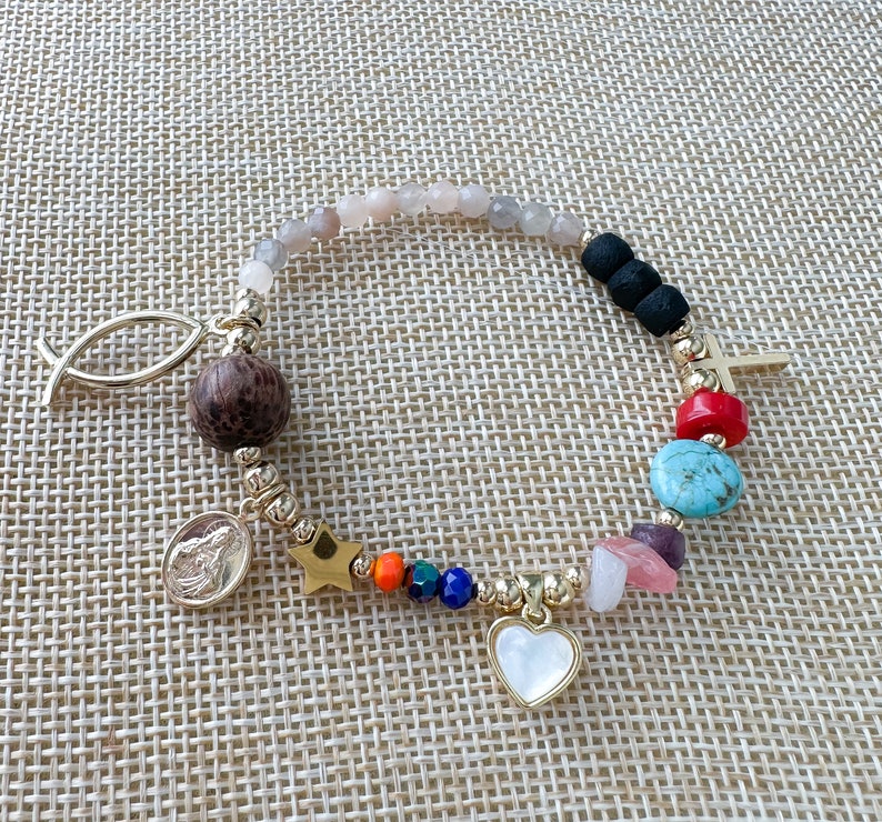 May include: A gold bracelet with a variety of charms, including a fish, a star, a heart, a cross, and several colorful beads. The bracelet is made of gold metal and has a delicate chain.