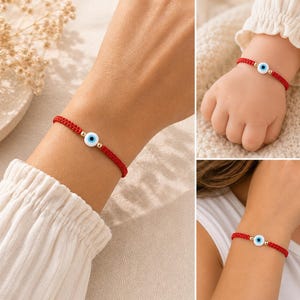 K&ouml;nnte beinhalten: Ein rotes Armband aus geflochtener Kordel mit einem zentralen, runden Nazar-Auge-Anh&auml;nger in Wei&szlig;, Blau und Schwarz, flankiert von zwei kleinen goldfarbenen Metallperlen. Das verstellbare Schnurarmband ist an verschiedenen Handgelenken zu sehen.