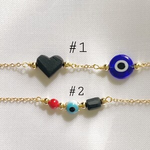 Puede incluir: Dos pulseras de cadena dorada. La pulsera n.&ordm; 1 tiene una cuenta negra en forma de coraz&oacute;n y una cuenta de ojo azul. La pulsera n.&ordm; 2 tiene una cuenta redonda roja, una cuenta de ojo azul claro y una cuenta cil&iacute;ndrica negra con cuentas doradas.