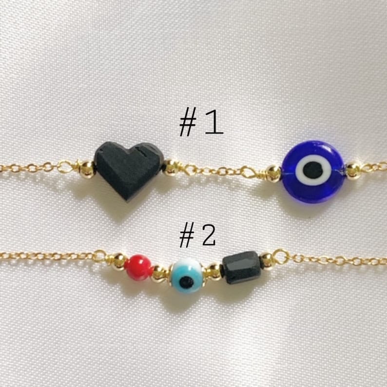 Puede incluir: Dos pulseras de cadena dorada. La pulsera n.&ordm; 1 tiene una cuenta negra en forma de coraz&oacute;n y una cuenta de ojo azul. La pulsera n.&ordm; 2 tiene una cuenta redonda roja, una cuenta de ojo azul claro y una cuenta cil&iacute;ndrica negra con cuentas doradas.