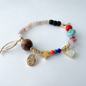 May include: A colorful beaded bracelet with a variety of charms, including a wooden bead, a star, a heart, and a religious medal. The bracelet is made with gold-toned beads and has a fish charm.